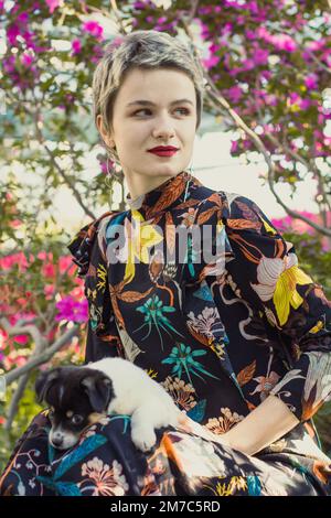 Gros plan femme élégante avec petit chiot en fleurs portrait de jardin Banque D'Images