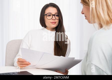 Jeune et belle agent d'assurance dans le client de conseil de lunettes et montre des documents Banque D'Images