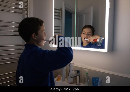 Garçon de 9 ans (modèle sorti) nettoyant ses dents à l'aide d'une brosse à dents électrique dans le miroir de la salle de bains avant d'aller à l'école, Londres, Angleterre Royaume-Uni Banque D'Images