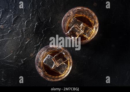 Whisky dans des verres avec glace. Whisky Bourbon sur des rochers sur fond de pierre noire, plan de pose à plat au-dessus Banque D'Images