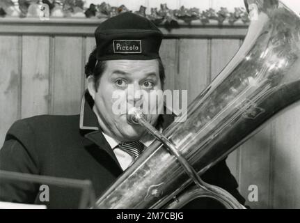 Homme jouant trombone avec le chapeau lisant Piccolo, film danois, 1960s Banque D'Images