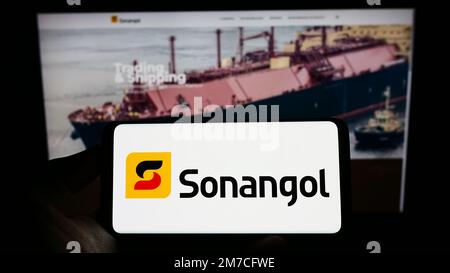 Personne tenant un téléphone portable avec le logo de la compagnie pétrolière angolaise Group Sonangol sur l'écran en face de la page web d'affaires. Mise au point sur l'affichage du téléphone. Banque D'Images