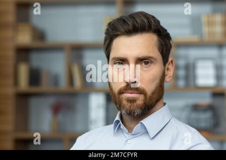 Gros plan photo d'un patron sérieux en chemise dans un bureau à domicile, homme mûr avec barbe regardant la pensée de la caméra, homme d'affaires tête d'impression investisseur. Banque D'Images