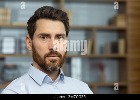 Gros plan photo d'un patron sérieux en chemise dans un bureau à domicile, homme mûr avec barbe regardant la pensée de la caméra, homme d'affaires tête d'impression investisseur. Banque D'Images