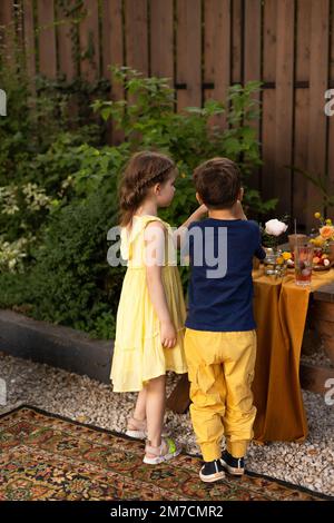 Enfants à la fête d'anniversaire, petite fille adorable et garçon avec boisson de limonade, en utilisant une paille, debout près de la table de fête d'anniversaire Banque D'Images