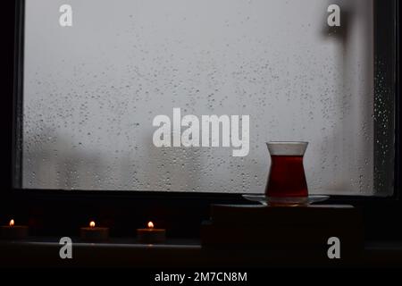Vue par une fenêtre avec des gouttes de pluie sur elle à d'autres maisons sur un jour pluvieux, thé, et bougies, Antalya, Turquie. Banque D'Images