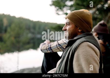 Vue latérale d'un homme souriant portant un chapeau en tricot par des amis Banque D'Images