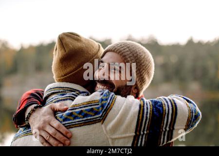 Des amis masculins heureux s'embrassent les uns les autres en portant des chapeaux en tricot Banque D'Images