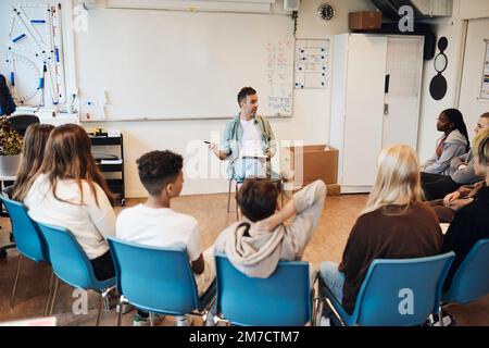 Professionnel de la santé mentale discutant avec des élèves de sexe masculin et féminin en thérapie de groupe à l'école Banque D'Images