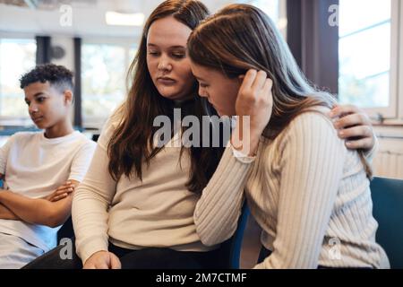 Triste adolescente assise avec le bras autour d'une amie femelle tout en la consolant dans la thérapie de groupe Banque D'Images