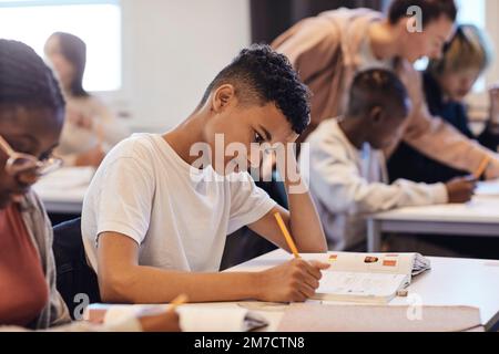 Ennuyé étudiant écrit dans le livre tout en étant assis par une amie femelle au bureau Banque D'Images