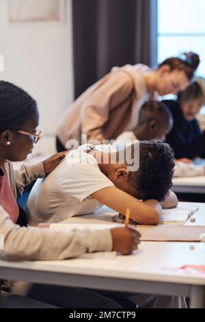 Une adolescente consolant un étudiant déprimé se reposant tête sur un bureau en classe Banque D'Images