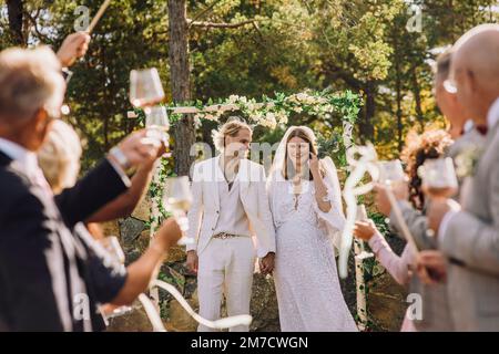 Happy bride and groom holding hands walking amidst guests at wedding Banque D'Images