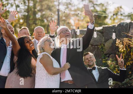 Heureux couple aîné récemment reçu prenant le selfie avec la famille et les amis par le biais de smartphone Banque D'Images