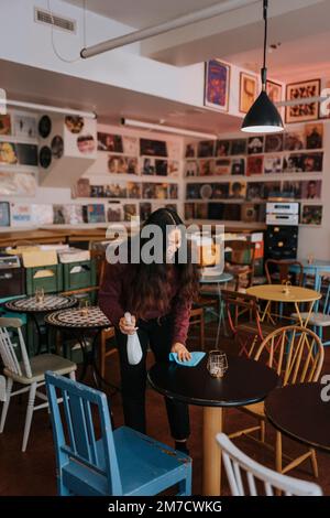 Femme entrepreneur souriante avec table de nettoyage de chiffon dans le café Banque D'Images