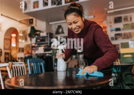 Une femme heureuse propriétaire de café avec un flacon pulvérisateur et une table de nettoyage de chiffon dans le café Banque D'Images