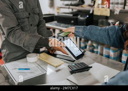 Un homme tient sur mesure un lecteur de carte de crédit tandis qu'un client féminin effectue un paiement sans contact en atelier Banque D'Images