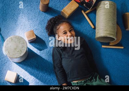 Portrait d'une fille souriante avec des jouets couchés sur un tapis au centre de garde d'enfants Banque D'Images