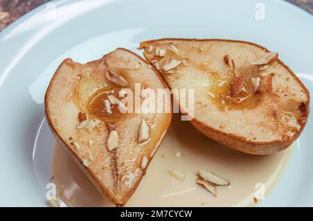 Poires cuites au miel avec amandes, cannelle, épices avec sauce sur plaque blanche. Banque D'Images