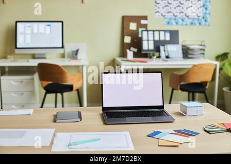 Image d'arrière-plan d'un intérieur de bureau confortable avec un espace de travail de conception et un écran blanc d'ordinateur portable ouvert sur le bureau, espace de copie Banque D'Images