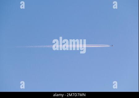Un avion à réaction passe au-dessus du ciel, laissant un sentier de vapeur fin à travers le ciel bleu clair. Banque D'Images