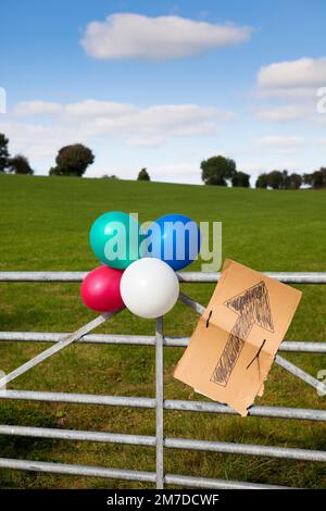 Ballons attachés avec une affiche en carton dans le pays, les points de signe avec une flèche et les ballons signifient qu'une partie est en cours et indique la direction dans laquelle elle est tenue. Banque D'Images