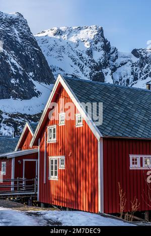 Chalets en bois rouge avec des montagnes enneigées en arrière-plan, Reine, comté de Nordland, îles Lofoten, Norvège Banque D'Images