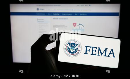 Personne tenant un téléphone cellulaire avec le sceau de l'Agence fédérale de gestion des urgences (FEMA) à l'écran devant la page Web. Mise au point sur l'affichage du téléphone. Banque D'Images