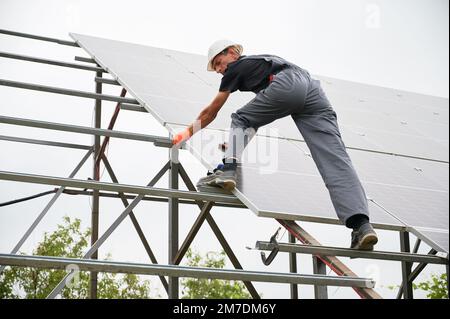 Homme technicien d'installation de panneaux solaires photovoltaïques. Homme travaillant dans un casque de sécurité plaçant le module solaire sur la structure de support lors du montage du système de panneaux photovoltaïques. Banque D'Images