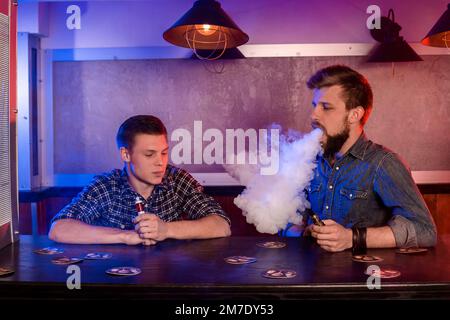 Homme vaping tenant un mod. Un nuage de vapeur au niveau du vapobar. Banque D'Images