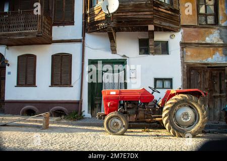 Un tracteur rouge devant des maisons de village de couleur jaune et blanche Banque D'Images