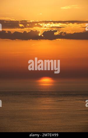 Des nuages et des conditions météorologiques spectaculaires à l'horizon au-dessus de la mer avec des reflets de la lumière du soleil sur la mer et des nuages roses profonds et colorés se reflétant dans l'eau de mer. Banque D'Images