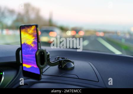 Téléphone mobile sur le tableau de bord d'une voiture au crépuscule avec les lumières d'autres véhicules sur la route Banque D'Images