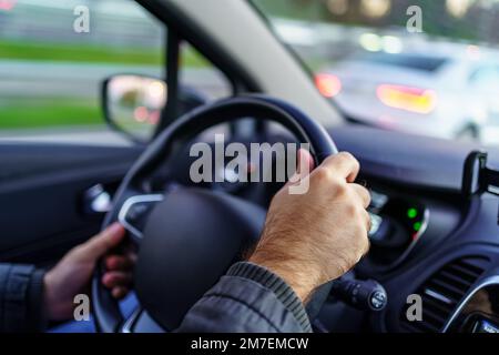 Les mains de l'homme conduisant la voiture la nuit avec les lumières hors foyer des autres véhicules sur la route. Banque D'Images