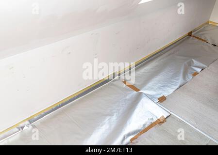 Mur sale dans diverses nuances de blanc préparé pour la peinture, le sol est recouvert de papier d'aluminium. Banque D'Images