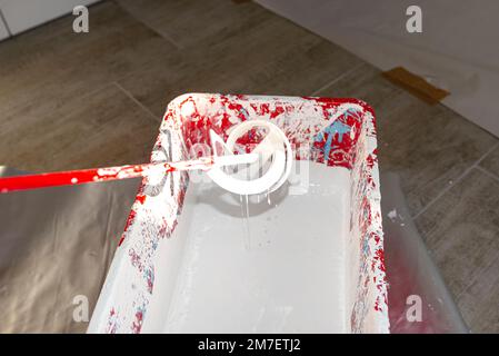 Un seau en plastique ouvert avec peinture blanche et un agitateur debout sur le sol. Banque D'Images