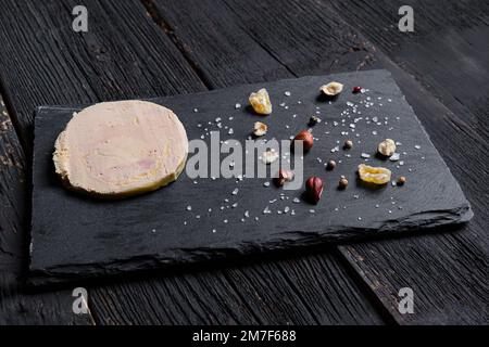 Foie gras traditionnel français sur une ardoise aux grains de poivre, noisettes, sel et fruits secs Banque D'Images