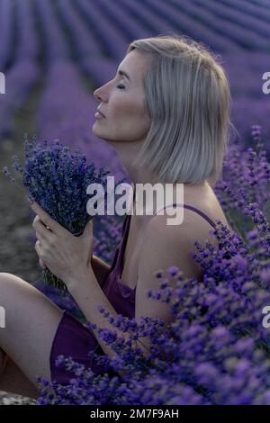 Une femme d'âge moyen est assise dans un champ de lavande et apprécie l'aromathérapie. Concept d'aromathérapie, huile de lavande, séance photo à la lavande Banque D'Images