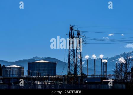 Paysage de production d'électricité avec cheminées de fumée, avec réservoirs de stockage de combustible de pétrole et pylônes d'électricité haute tension dans la silhouette sur ciel bleu an Banque D'Images