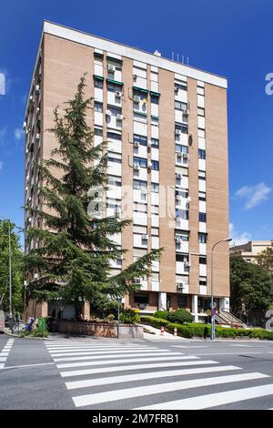 Façade d'un bâtiment avec des jardins, des arbres, un portail en métal noir et une rampe d'accès au garage adjacent vu de l'autre côté de la rue sur un Banque D'Images