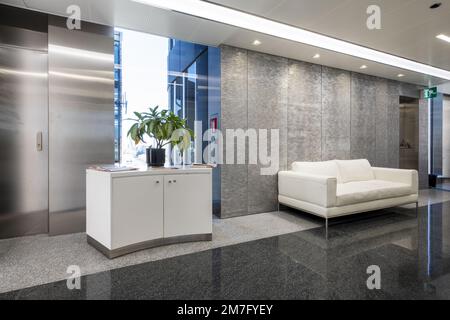 Hall d'entrée d'un bureau dans un immeuble de bureaux avec planchers de granit poli à deux tons et canapés en cuir blanc Banque D'Images