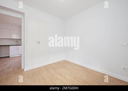 Cette chambre vide dispose d''une armoire intégrée avec deux vieilles portes blanches avec plinthes, parquet, murs blancs lisses et accès à un k meublé Banque D'Images