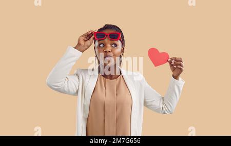 Femme noire stupéfaite tient le coeur en papier rouge dans les mains Banque D'Images