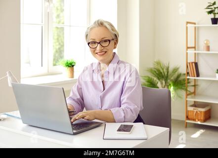 Femme d'âge moyen assise au bureau et travaillant avec un ordinateur portable Banque D'Images