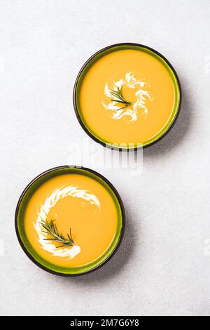 Deux bols verts avec une épaisse bisque de courge musquée garni de crème épaisse et de romarin sur une table en béton léger. Bol de citrouille et crème de carottes Banque D'Images