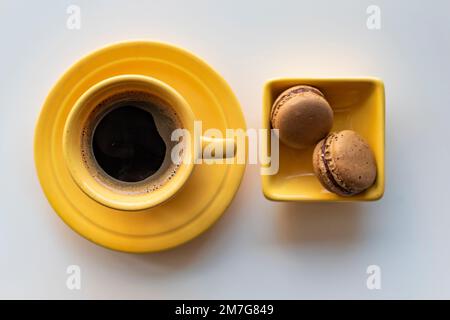 Angle supérieur d'une tasse jaune de café noir et de deux macarons sur fond blanc Banque D'Images