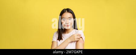 Covid-19 et le concept médical de santé.Une jeune fille coréenne souriante montre l'épaule avec un timbre, a pris une injection de vaccin coronavirus pendant une pandémie, jaune Banque D'Images