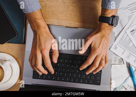 Vue de dessus de l'homme dactylographiant sur l'ordinateur portable, remplir les taxes, comptabilité, saison d'imposition. Banque D'Images
