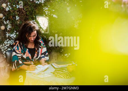 Femme adulte caucasienne artiste faisant un dessin aquarelle assis à une table sur la terrasse de sa maison, art et concept d'école, espace de copie. Banque D'Images