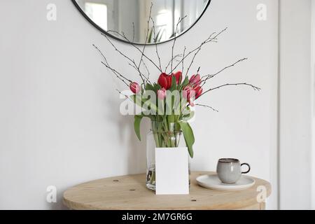 Décoration de printemps de Pâques. Bouquet de tulipes roses et branches de bouleau dans un vase en verre. Maquette de carte de vœux vierge. Tasse de café, bois d'époque Banque D'Images